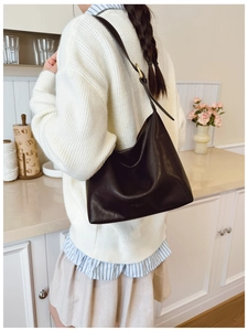 Detail of a dark coffee leather hobo bag showing glossy texture and gold hardware accents