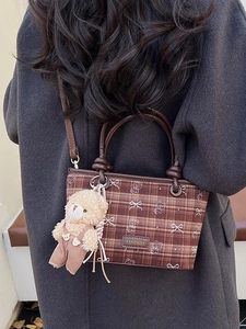 Brown plaid bucket bag with plush bear charm worn by a model in a grey coat