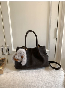 Detail of dark grey suede tote bag featuring a plush rabbit pendant and shoulder strap