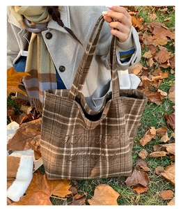 Close-up of vintage plaid embroidery on brown wool tote bag with autumn leaf background