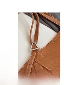 Close-up of brown litchi leather bag showing silver triangle buckle and white stitching