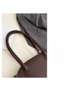 Detailed macro view of brown pebbled leather texture and wide shoulder strap on tote bag