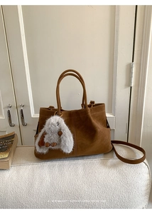 Close-up of brown suede handbag with a plush rabbit charm on a cream sofa