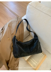 Détail d'un sac à bandoulière vintage en cuir noir avec ferrures dorées sur un canapé