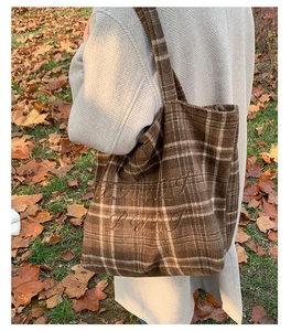 Detailed close-up of brown plaid embroidery tote bag with LUBI text on autumn leaves