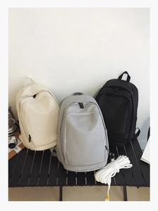 Three waterproof soft leather backpacks in beige, grey, and black on an outdoor table