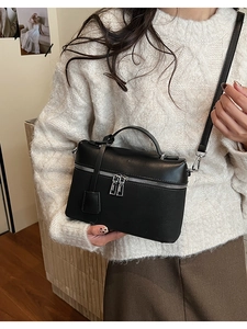 Detail of a black leather crossbody bag on a model wearing a white knit sweater