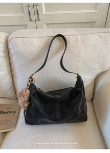 Détail d'un sac cabas noir vintage avec charm en peluche sur un canapé douillet
