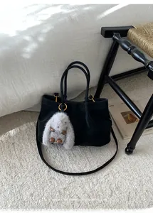 Detail of minimalist black suede tote bag featuring a grey plush bunny charm and gold hardware