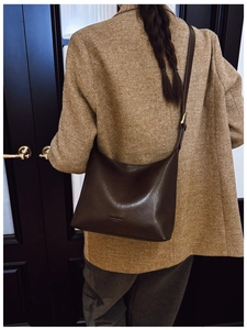 Detail of dark brown leather hobo bag with adjustable strap against vintage door