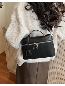 Rear view of a black leather Boston bag being worn with a white knit sweater and brown skirt