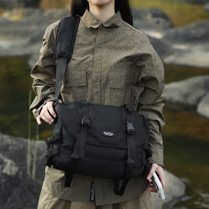 Close-up of black waterproof nylon messenger bag with buckle straps in outdoor setting
