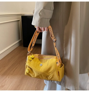 Detail of bright yellow crossbody bag with branded wide strap shown on a trench coat