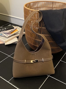 Brown leather hobo tote bag with gold buckle and white contrast stitching in a cozy setting