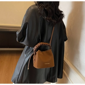 Brown leather bucket bag with woven handle and gold logo detail shown on model