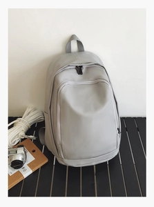 Detail of light gray waterproof backpack featuring front zipper pocket on dark table