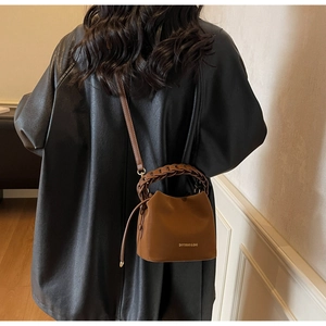 Detail of a brown leather bucket bag with wide woven handle and adjustable strap