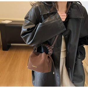 Detail of a dark brown mini bucket bag with textured fabric and a braided handle