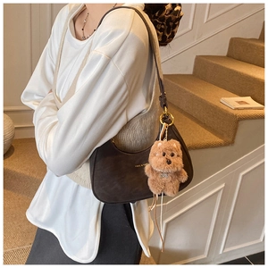 Close-up of dark brown suede crescent bag with gold logo and plush puppy charm detail