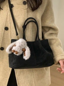 Black faux suede handbag with plush bunny charm shown on a textured beige coat