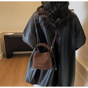 Close-up of brown leather bucket bag with braided handle and gold brand logo detail
