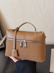 Brown textured leather crossbody bag with dual zippers and single handle on a wooden background