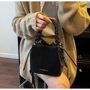 Detail of black drawstring bucket bag with gold chain handle and brand lettering