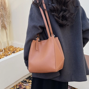 Brown lychee leather tote bag with geometric design worn by model in an autumn setting