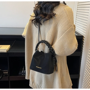 Detail of a chic black bucket bag with a chunky chain handle worn over the shoulder