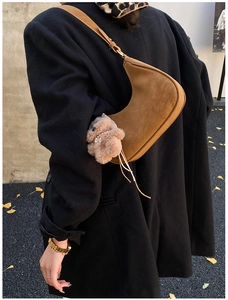 Detail of a brown suede half-moon underarm bag with a plush animal charm on a shoulder strap