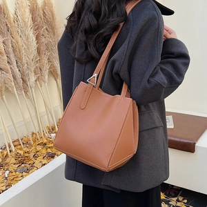 Brown lychee leather tote bag with silver triangle hardware detail on a warm winter coat