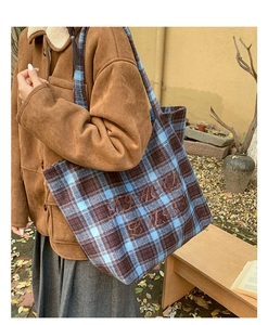 Detailed view of large plaid canvas tote bag with embroidered letters in a winter setting