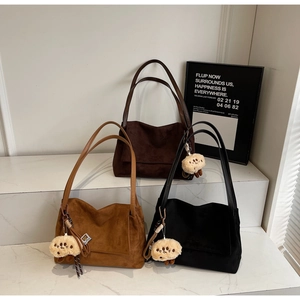 Detailed close-up of three suede tote bags in coffee, tan, and black with plush charms