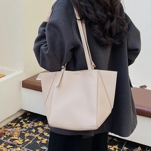 Rear view of a model carrying a beige litchi grain tote bag in an autumn park setting