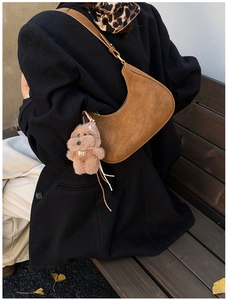 Brown suede hobo bag with a cute teddy bear charm shown on a rustic wooden bench