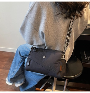 Close-up of black crossbody bag with multi-pocket design and contrast letter strap