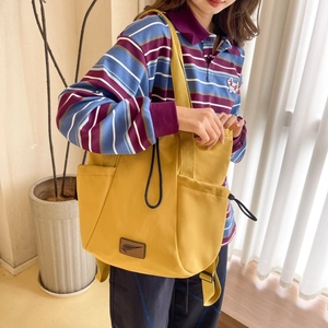 Detail of a bright yellow nylon drawstring backpack with side pockets and leather brand tag
