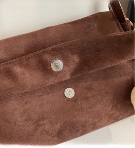Detail of magnetic hardware closure and suede texture on dark brown tote bag
