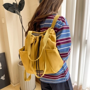 Rear view of model wearing a yellow nylon backpack with drawstring and side pocket