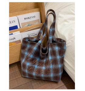 Detail of wool plaid tote bag with brown embroidery on textured autumn fabric