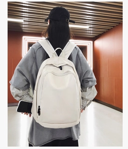 Minimalist white PU leather backpack with large front pocket shown on model's back