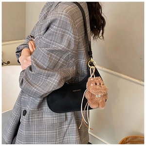 Detail of black leather crescent underarm bag with a brown plush bear charm accessory