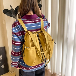 Detail view of the yellow drawstring backpack worn by a model in a casual home setting