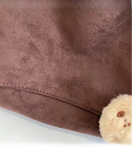 Detail of dark brown suede bag with embossed logo texture and soft plush pendant