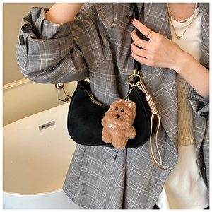 Close-up of black crescent shoulder bag with plush bear charm and woven tassel detail