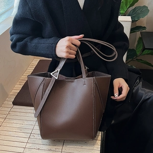 Detail of dark brown lychee leather tote bag featuring triangle metal buckle and white stitching
