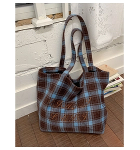 Detailed macro view of the woven plaid wool fabric and embroidered logo on the tote bag