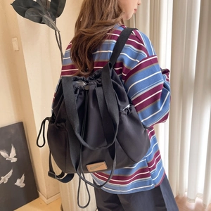 Detail of a black nylon drawstring backpack featuring a leather patch in a home setting