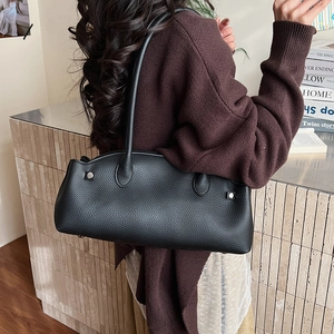 Detail of black lychee grain leather shoulder bag with silver buckle on a model