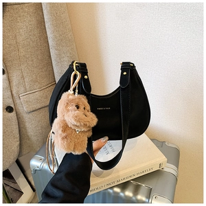 Detail of black leather crescent underarm bag featuring a cute plush bear pendant accessory